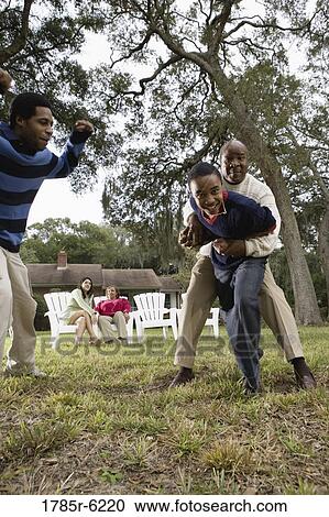 Stock Image - Father and sons wrestling playfully in backyard. Fotosearch