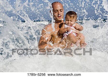 Stock Photograph - Father playing with baby girl in the ocean waves. Fotosearch