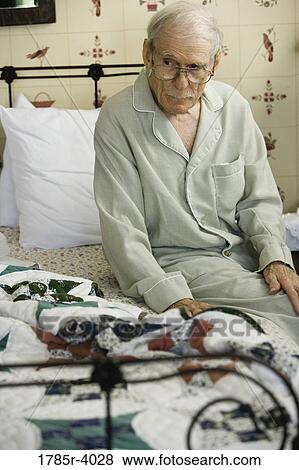 Stock Photo - Feeble senior man sitting on edge of bed. Fotosearch