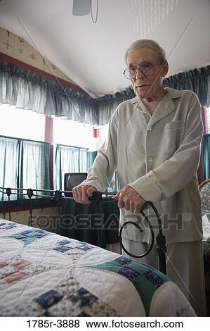 Stock Photo - Feeble senior man trying to walk while holding on to bedframe. Fotosearch