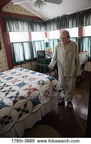 Feeble senior man trying to walk while holding on to bedframe View Large Photo Image Stock Photo - Feeble senior man trying to walk while holding on to bedframe. Fotosearch