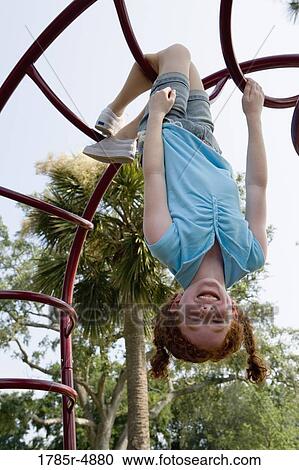 Stock Image - Girl hanging upside-down from jungle gym at a playground. Fotosearch
