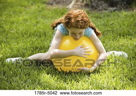Stock Image - Girl lying on top of a big inflated yellow ball. Fotosearch