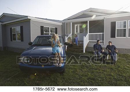 Stock Image - Girl sitting on hood of old truck playing patty-cake, family in background. Fotosearch