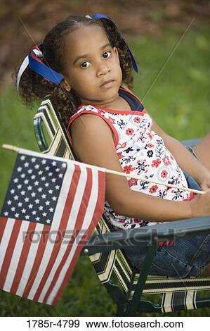 Stock Photo - Girl sitting on the chair waving US flag. Fotosearch