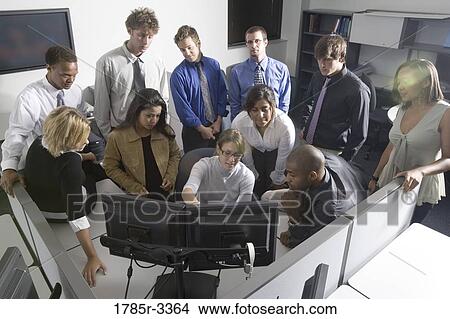 Picture - Group of young workers in office gathered around computer screen. Fotosearch