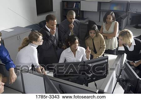 Stock Image - Group of young workers in office gathered around computer screen. Fotosearch