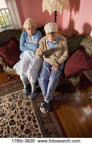 Grumpy senior couple sitting on sofa in living room View Large Photo Image Stock Image - Grumpy senior couple sitting on sofa in living room. Fotosearch