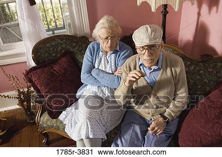 Stock Image - Grumpy senior couple sitting on sofa in living room. Fotosearch