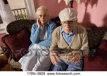 Stock Photo - Grumpy senior couple sitting on sofa in living room. Fotosearch