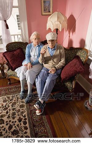 Stock Photo - Grumpy senior couple sitting on sofa in living room. Fotosearch