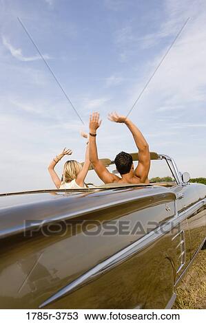 Happy, cheerful and waving young couple sitting in antique convertible car View Large Photo Image Stock Image - Happy, cheerful and waving young couple sitting in antique convertible car. Fotosearch