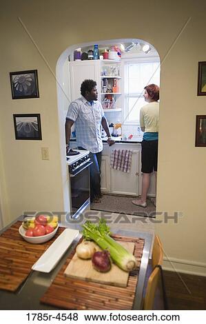 Stock Photo - Inter-racial couple talking in kitchen with kitchen table in foreground. Fotosearch