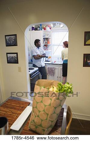 Inter-racial couple talking in kitchen with bag of groceries in foreground View Large Photo Image Stock Photograph - Inter-racial couple talking in kitchen with bag of groceries in foreground. Fotosearch