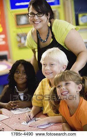 Stock Image - Kids posing and smiling with their teacher in a colorful classroom. Fotosearch