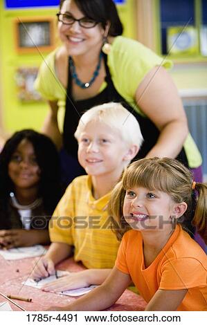 Kids posing and smiling with their teacher in a colorful classroom View Large Photo Image Stock Image - Kids posing and smiling with their teacher in a colorful classroom. Fotosearch