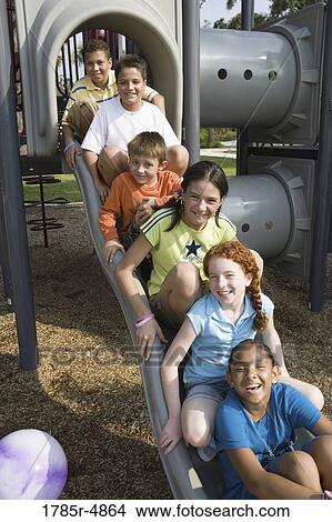 Picture - Laughing children sitting on a slide at a playground. Fotosearch