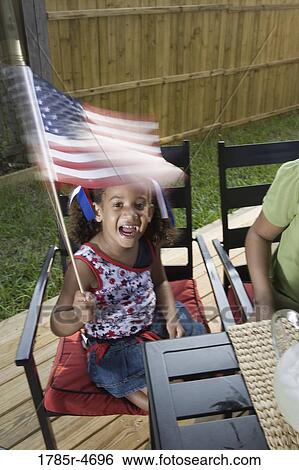 Stock Photograph - Little girl at 4th of July cookout waving American flag. Fotosearch