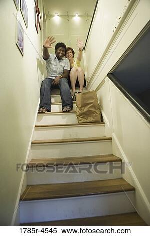 Stock Photography - Low angle view of a young inter-racial couple sitting on top of a stairway waving. Fotosearch