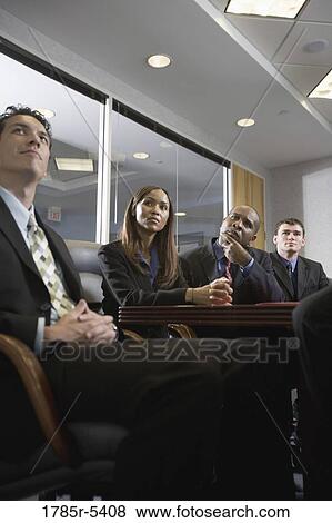 Low angle view of business men and women watching and listening attentively in a formal conference room View Large Photo Image Stock Photo - Low angle view of business men and women watching and listening attentively in a formal conference room. Fotosearch