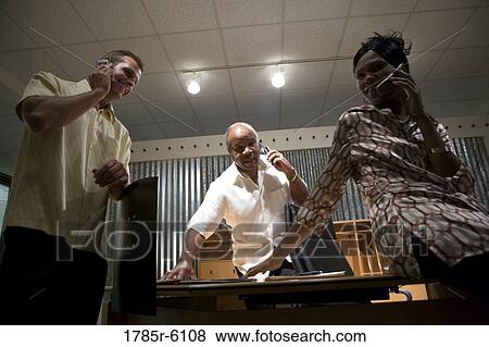 Low angle view of three business people on their mobile phones in an office View Large Photo Image Stock Photo - Low angle view of three business people on their mobile phones in an office. Fotosearch