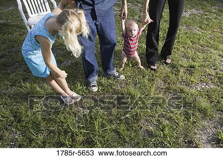 Stock Image - Lower portion of portrait of blue-collar family standing on grass. Fotosearch