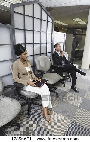 Stock Image - Man and woman sitting in an office waiting area. Fotosearch