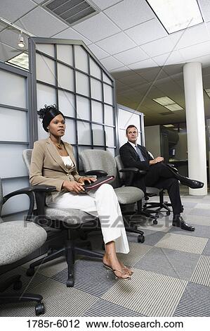 Stock Image - Man and woman sitting in an office waiting area. Fotosearch