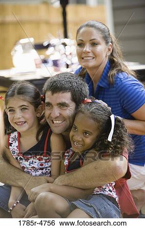 Stock Photograph - Man closely hugging two giggling young girls with woman in background. Fotosearch