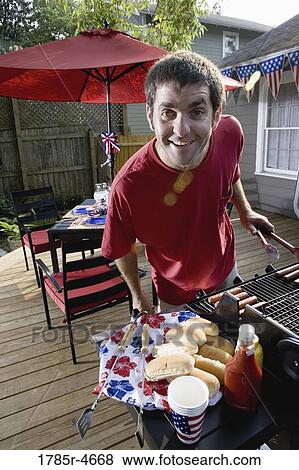Man grilling hot dogs in backyard patio with picnic table and 4th of July decoration in background View Large Photo Image Stock Photo - Man grilling hot dogs in backyard patio with picnic table and 4th of July decoration in background. Fotosearch