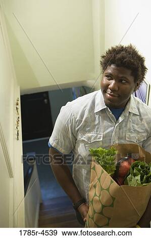 Man holding a grocery bag filled with groceries View Large Photo Image Stock Photo - Man holding a grocery bag filled with groceries. Fotosearch