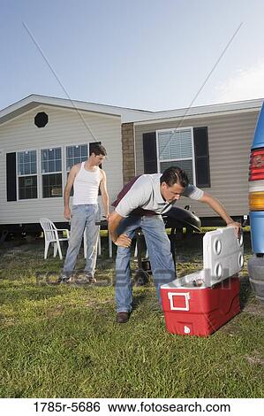 Man looking into ice chest while another man watches, in front of trailer home View Large Photo Image Stock Photograph - Man looking into ice chest while another man watches, in front of trailer home. Fotosearch