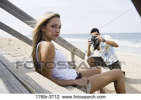 Stock Image - Man photographing a woman at the beach. Fotosearch
