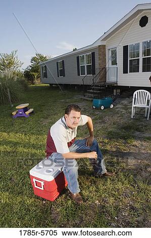 Man sitting on an ice chest holding a drink bottle in front of trailer home View Large Photo Image Stock Photography - Man sitting on an ice chest holding a drink bottle in front of trailer home. Fotosearch
