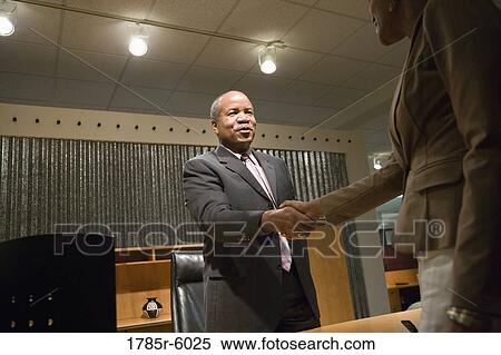 Mature business man standing behind desk shaking hands with younger woman View Large Photo Image Stock Photography - Mature business man standing behind desk shaking hands with younger woman. Fotosearch
