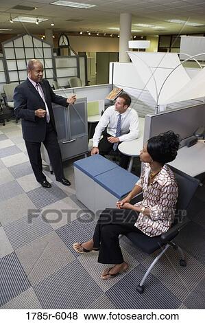 Mature businessman conversing with associates in office cubicles View Large Photo Image Stock Photo - Mature businessman conversing with associates in office cubicles. Fotosearch