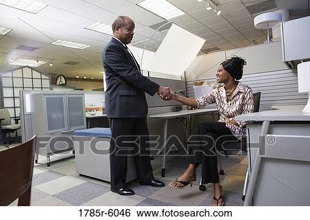 Mature businessman shaking hands with younger woman sitting in a new office cubicle View Large Photo Image Stock Photograph - Mature businessman shaking hands with younger woman sitting in a new office cubicle. Fotosearch
