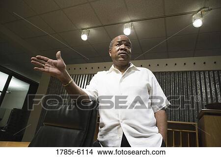 Mature businessman standing behind his desk gesturing towards the viewer View Large Photo Image Picture - Mature businessman standing behind his desk gesturing towards the viewer. Fotosearch