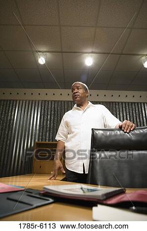 Stock Image - Mature businessman standing behind his desk. Fotosearch