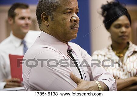 Mature businessman with younger colleagues in background View Large Photo Image Stock Photo - Mature businessman with younger colleagues in background. Fotosearch