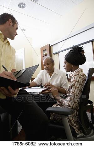Mature businessman working closely with younger man and woman in a conference room View Large Photo Image Stock Image - Mature businessman working closely with younger man and woman in a conference room. Fotosearch