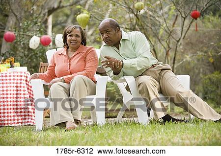 Stock Image - Mature couple conversing next to picnic table. Fotosearch