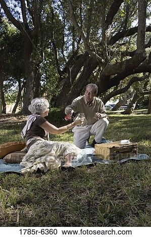 Mature couple enjoying wine on picnic blanket View Large Photo Image Stock Image - Mature couple enjoying wine on picnic blanket. Fotosearch