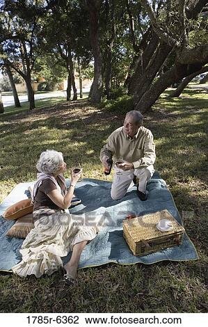 Stock Image - Mature couple having a picnic enjoying wine. Fotosearch