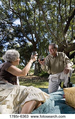 Stock Image - Mature couple having a picnic enjoying wine. Fotosearch