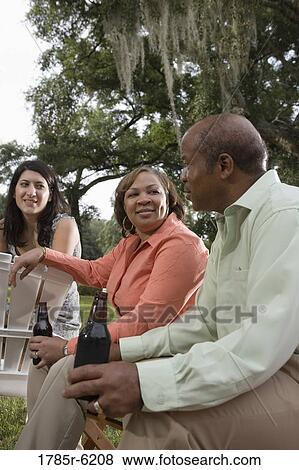Mature couple having drinks sitting on lawn chairs next to young woman View Large Photo Image Stock Photo - Mature couple having drinks sitting on lawn chairs next to young woman. Fotosearch