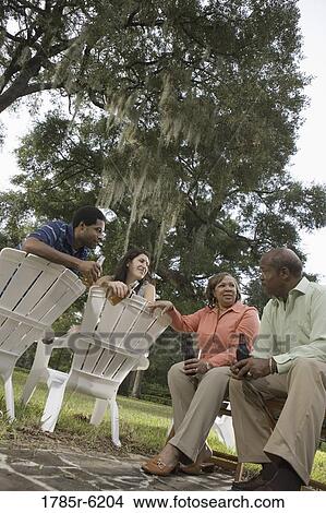Picture - Mature couple having drinks with inter-racial couple while sitting on lawn chairs. Fotosearch