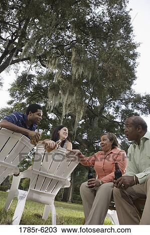 Stock Image - Mature couple having drinks with inter-racial couple while sitting on lawn chairs. Fotosearch