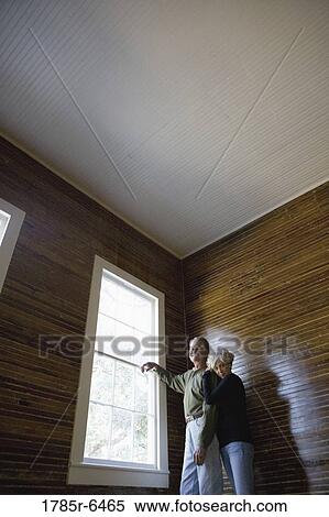 Stock Photography - Mature couple in a darkened room leaning against window, gazing out. Fotosearch