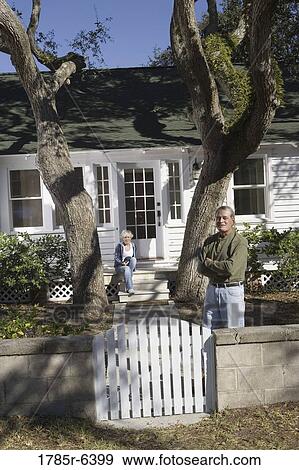 Stock Photo - Mature couple in front of house surrounded by tall oak trees. Fotosearch